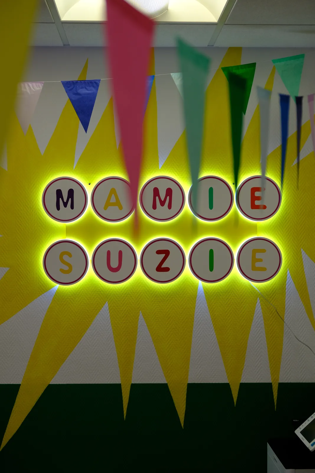 L'enseigne lumineuse Mamie Suzie sur le grand soleil jaune peint au mur