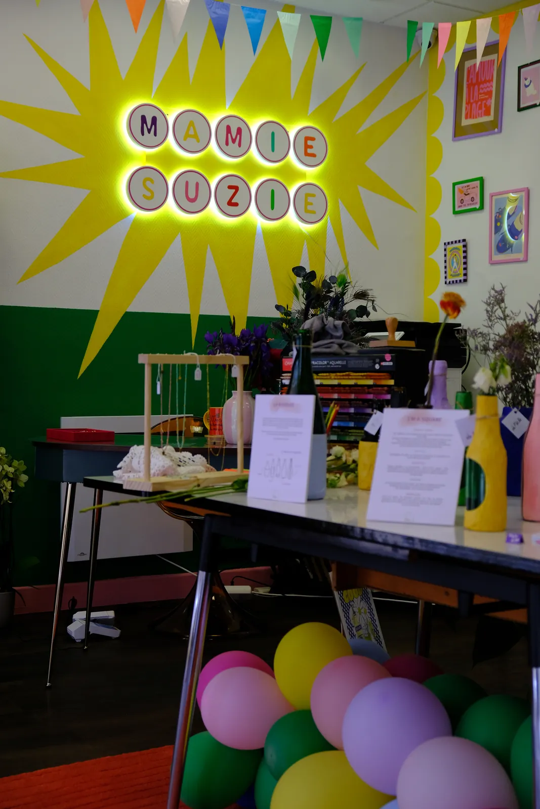 L'intérieur de la boutique avec l'enseigne lumineuse Mamie Suzie, des fanions et des ballons colorés